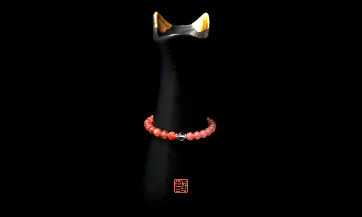 Wearable Feng Shui crystal bracelet with strawberry quartz and clear quartz beads displayed on a black ceramic stand, symbolizing personal energy signature and the balance of mind and emotions - JING Balance