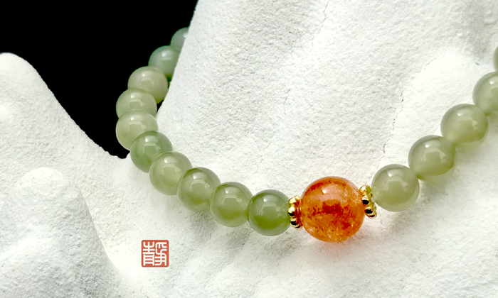 Wearable Feng Shui crystal bracelet featuring green jade and sunstone beads with natural inclusions, photographed on a white stone background, symbolizing the beauty and meaning of natural crystal imperfections- JING Balance