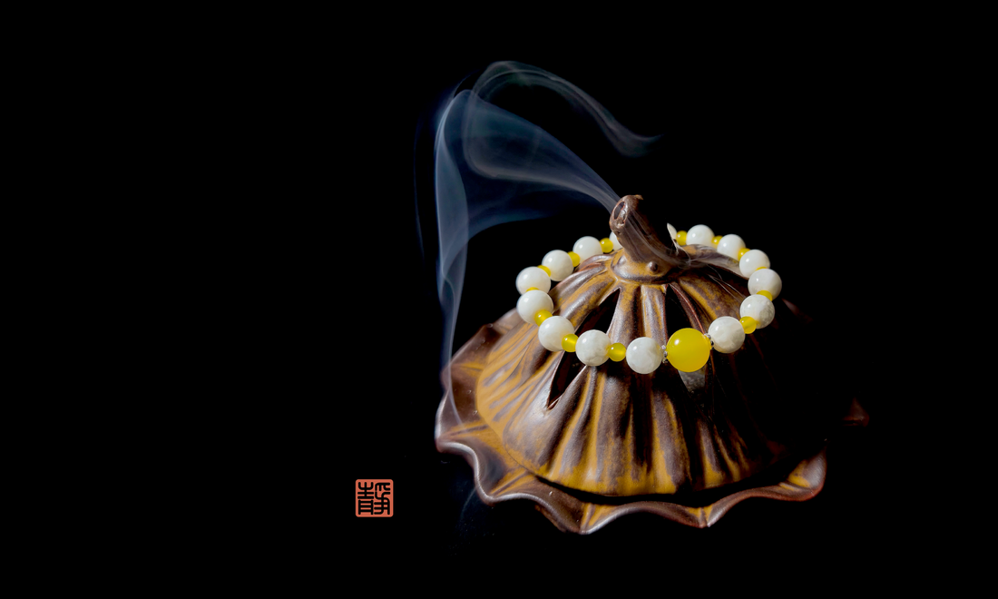 Wearable Feng Shui crystal bracelet in yellow jade and white jade placed on a ceramic incense burner with rising smoke, symbolizing gentle crystal cleansing and energy reset.
