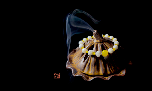 Wearable Feng Shui crystal bracelet in yellow jade and white jade placed on a ceramic incense burner with rising smoke, symbolizing gentle crystal cleansing and energy reset.